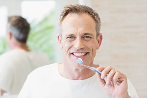 A middle-aged man using a manual toothbrush to clean his teeth in Bedford