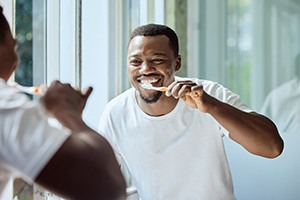 smiling man brushing his teeth in front of a mirror