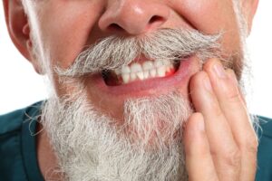 Nose-to-chin view of white bearded/mustached man holding his hand up to his red, swollen gums