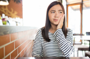 Woman at a restaurant rubbing her jaw and looking to the side